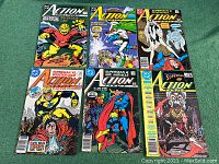 All six Action Comics issues displayed together on green surface showing front covers, highlighting main characters and titles.