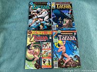Four vintage Tarzan comic books laid out flat on green fabric background showing full covers from DC and Marvel publishers around 1973-1977.