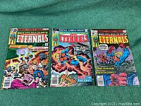 Three comic books: The Eternals No. 2, 3, and 16 laid out side by side showing full front covers on green fabric background.