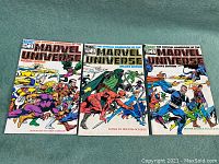 Three Marvel Comics from 1983: The Official Handbook of the Marvel Universe Deluxe Edition issues #1, #3, and #4 laid out showing their front covers with multiple Marvel superheroes and villains.