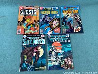 Five vintage 1970s DC horror comics arranged on a blue surface: Ghosts, two Secrets of Haunted House issues, House of Secrets, and Weird Mystery Tales.