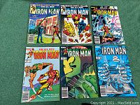 Top down view of all six Iron Man comic books in the lot laid out in two rows of three on a green fabric surface.