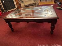 Front angle showing the table with X-shaped glass insets on top, wooden border, and visible scratches.