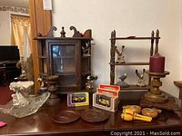 Photo showing wooden display case, display shelf, eagle figurines, boxed model cars, wooden candle holders, maracas, small wooden plates, and a decorative glass bowl arranged on a wooden surface.