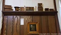 Miniature wooden dollhouse furniture pieces arranged on a wooden shelf, showing various dressers, cabinets and chests in natural wood finish with some dust.