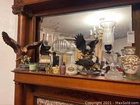 Eagle figurines, candle holders, candles, trinket box, and decorative vase arranged on a wooden furniture piece with mirror.