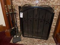 Photo showing two black metal fireplace screens, one with broken frame, and the fireplace tools set and log rack beside them.