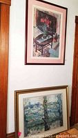 Two framed art prints displayed leaning against a wall and hanging, showing floral and landscape themes.
