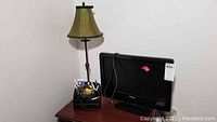 Photo of brass table lamp, Philips TV, and desk organizer with office supplies on wooden table