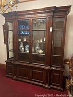 Front view of large wooden lighted wall unit china cabinet showing glass display doors with various decorative items inside and solid wood cabinet doors below.