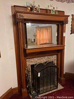 Front view of large wooden fireplace mantelpiece with mirror and decorative columns surrounding the fireplace opening.