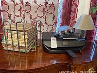 Overall view of the printer, lamp, books stacked in metal holder on a wooden surface