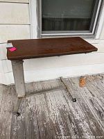 Full view of rolling bedside table with brown laminate top and metal base showing wear and rust