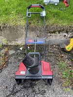 Front view of Toro Power Curve 1800 electric snow thrower showing red and black plastic body with black snow discharge chute and metal handlebar.