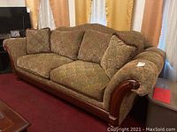 Angled view of the sofa showing the wooden base, curved armrests, patterned fabric cushions with visible wear, and overall shape.