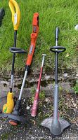 Three string trimmers laid out on grass showing different designs and colors