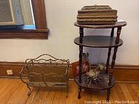 Wood 3-tier table, ornate decorative box on top, framed picture, candle holder, and metal magazine rack on floor nearby