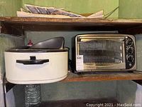 Both GE toaster and Rival roaster oven on a wooden shelf, side by side showing their exterior condition.