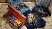 Overview of toolbox, carrying case, and two tool bags filled with various hand tools on tiled floor