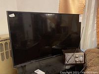 Vizio TV and Curtis radio on a black surface with curtains in the background.