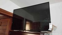 Front view of the RCA flat screen TV showing screen and black frame with a black base stand on a wooden surface.