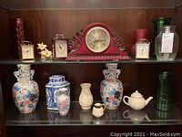 Wide view of glassware, clocks and ceramics on shelves including red wooden mantel clock, glass vases, ceramic floral vases and teapots.