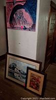 Three pieces of wall art shown; an unframed architectural piece on the wall and two framed prints leaning against the wall.