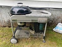 Full front view of the Weber Performer charcoal grill with side table on grass outdoors, grill base has wire rack and wheels.