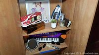 Wooden cabinet shelves with boxed Yankee Candle mini jars, toy keyboard, jewelry box, CDs, sunglasses, mirror, succulent plant, and assorted candles
