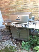 Front view of stainless steel propane barbecue grill with lid closed, control knobs and storage cabinet below.