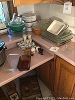 Wide view of countertop with stacked glass Pyrex casserole dishes, white ceramic casserole, green glass mixing bowls, small white egg holders, salt and pepper shakers, and other small dishes.