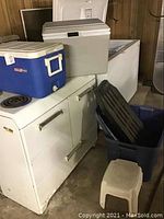 Wide shot showing all items: coolers on top of stove, tote container with dolly inside, and small stool on floor.