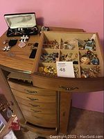 Collection of costume jewelry spread in a wooden divider on top of a dresser, including earrings, brooches, pins, and other small pieces.