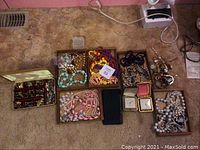 Overview of lot showing multiple trays and boxes containing colorful beaded necklaces, bracelets, small watches, and earrings arranged on carpeted floor.
