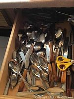 Drawer with mixed forks, spoons, knives and scissors, showing wooden and metal handles.