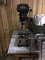 Front view of Job Mate drill press on a white table against a wood-paneled wall.