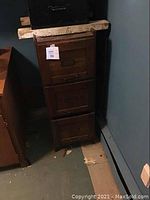 Front view of the tall wooden filing cabinet with 3 drawers showing its height and handles.