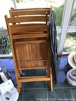 Four wooden folding chairs stacked together; natural wood color, slatted seats and backs