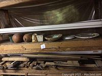 Various flower pots, decorative bowls, glass water jug, and plates arranged on wooden shelving showing scratches and use
