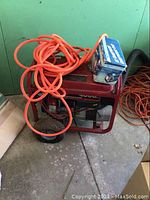 Front and top view of red-framed generator with coiled orange cord and compressor box on top