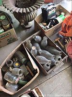Cardboard box filled with various vintage glass bottles with some metal and wooden tools near them