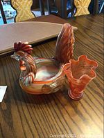 Glass rooster figurine and flared glass vase on wood table