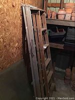 Photo showing two ladders leaning against a wooden wall in a storage room, one wooden and one metal.