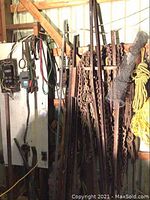 Display of rusted metal rods, pipes, heavy-duty chains, metal hooks, and rolled chicken wire against a warehouse wall.