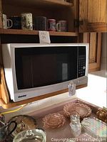 Front and side view of Danby microwave on wooden shelf with glass and ceramic kitchenware around.