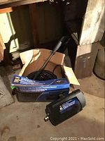 Photo showing power fist pressure washer motor housing, hose coiled inside a cardboard box, and spray wand.