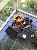 Full view of reciprocating saw placed inside hard plastic carrying case, with two extension cords coiled inside.