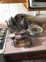 Full view of all silver plated items on countertop including teapots, trays, bowls, and cream and sugar set.