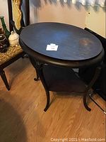 Photo showing the wooden oval tabletop and part of the carved legs, reflecting the table's dark finish and weathered surface.