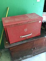 Red metal tool chest with closed lid placed on wooden cabinet